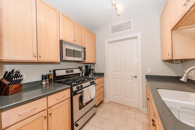 kitchen with visible vents, a sink, light brown cabinetry, stainless steel appliances, and dark countertops