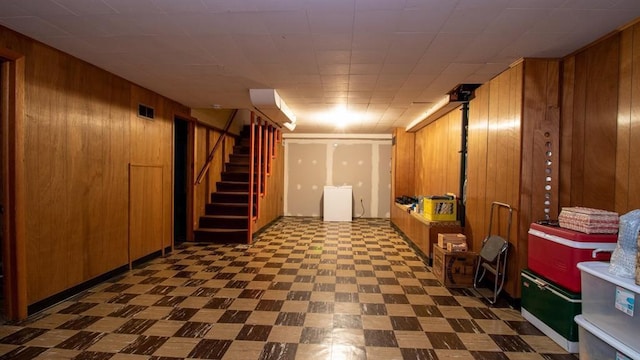 finished below grade area with tile patterned floors, stairway, wooden walls, and visible vents