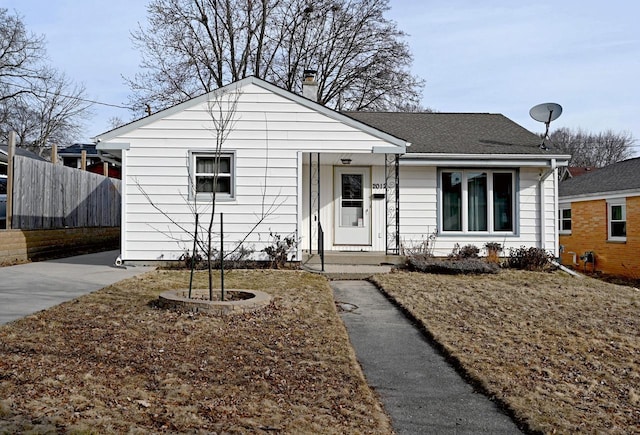 bungalow-style home featuring a chimney, roof with shingles, and fence