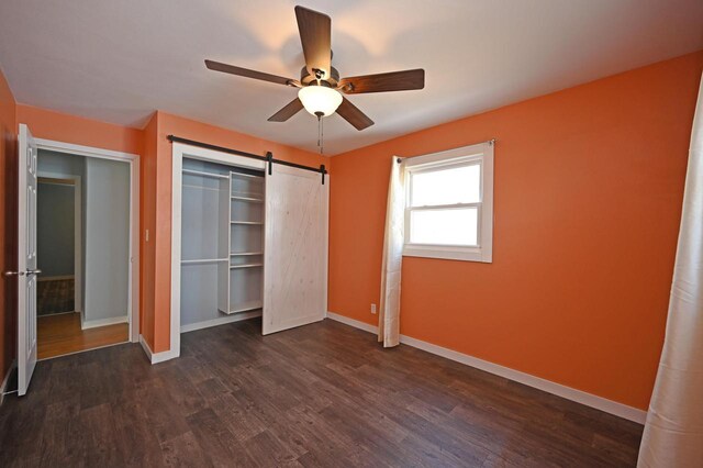 unfurnished bedroom with a barn door, a closet, baseboards, and dark wood-style flooring