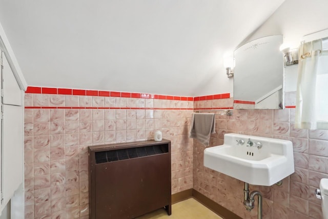 bathroom with toilet, wainscoting, heating unit, tile walls, and a sink