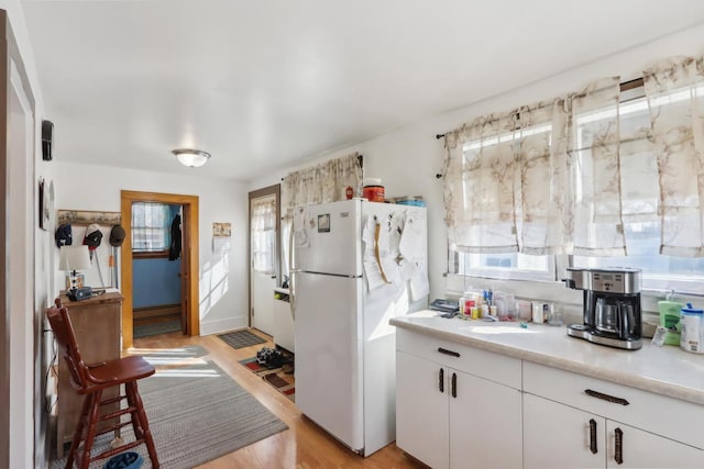 kitchen featuring white cabinetry, light countertops, freestanding refrigerator, and a baseboard radiator