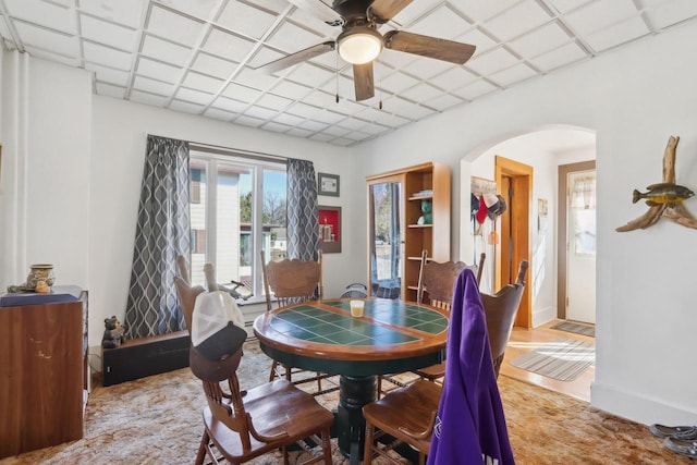 dining room featuring carpet floors, arched walkways, a drop ceiling, and ceiling fan