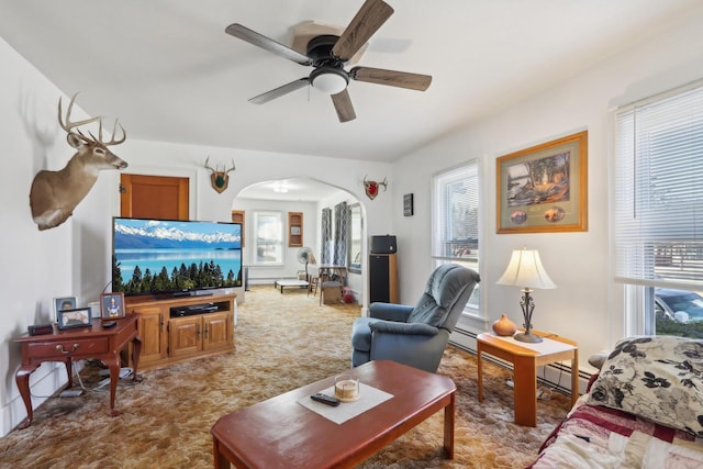 carpeted living room featuring arched walkways, a baseboard heating unit, and a ceiling fan