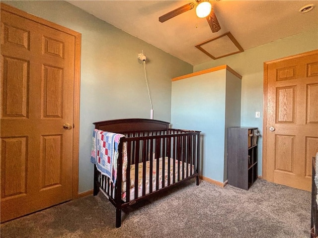 bedroom featuring a nursery area, carpet, baseboards, attic access, and ceiling fan