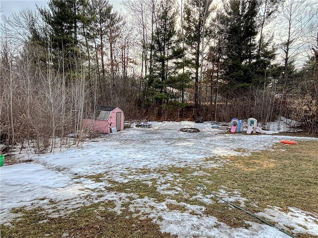 yard covered in snow with an outbuilding, a playground, and a storage unit