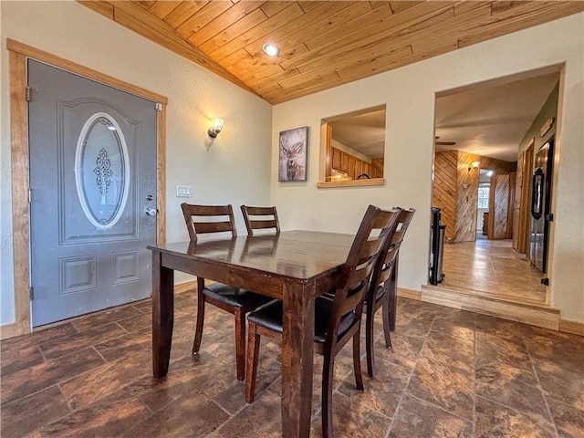 dining area with stone finish floor, wooden walls, baseboards, wood ceiling, and ceiling fan