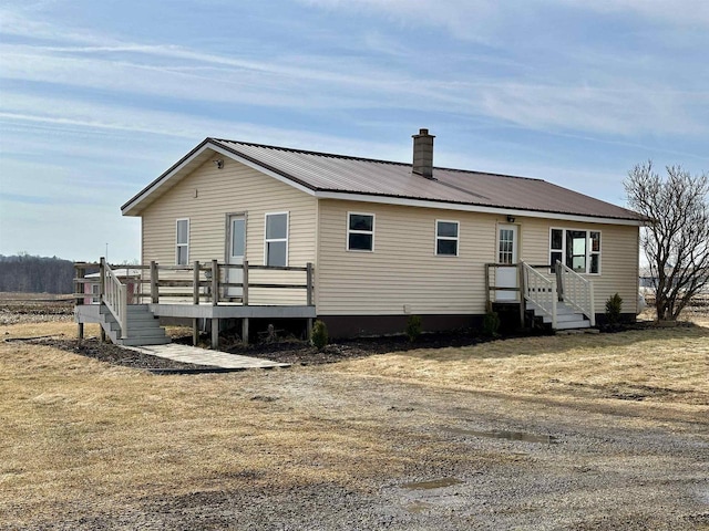 rear view of property featuring metal roof, a deck, and a chimney