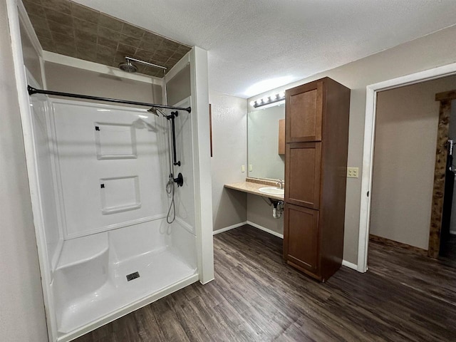 bathroom featuring wood finished floors, baseboards, a sink, a shower, and a textured ceiling