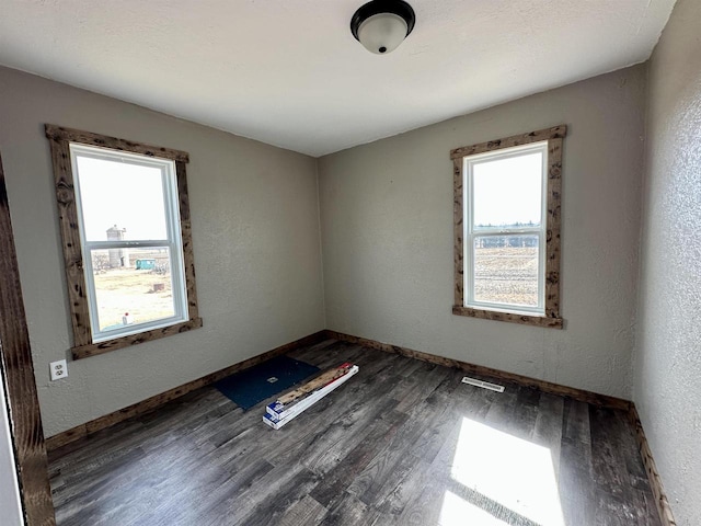 spare room featuring visible vents, wood finished floors, baseboards, and a textured wall