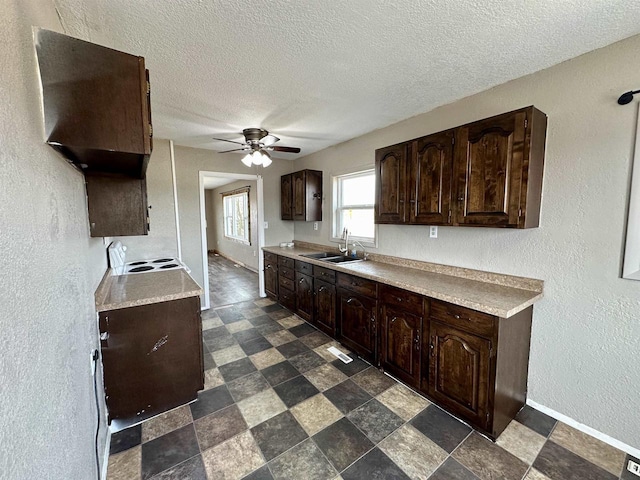 kitchen featuring ceiling fan, light countertops, dark brown cabinets, and a sink