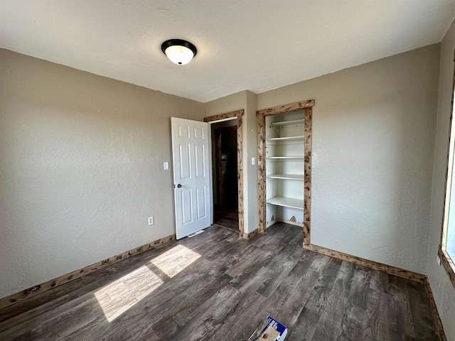 unfurnished bedroom featuring a closet, baseboards, dark wood-type flooring, and a textured wall