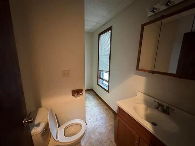 bathroom with vanity, toilet, a paneled ceiling, and baseboards