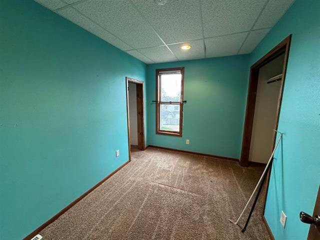 unfurnished bedroom featuring a drop ceiling, carpet flooring, and baseboards