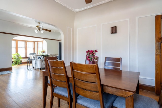 dining space with wood finished floors, a ceiling fan, arched walkways, and ornamental molding