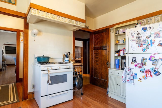 kitchen with white appliances, arched walkways, and wood finished floors