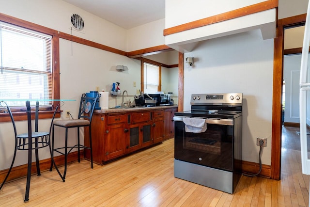 kitchen featuring baseboards, light wood-style flooring, stainless steel electric range, brown cabinets, and a sink