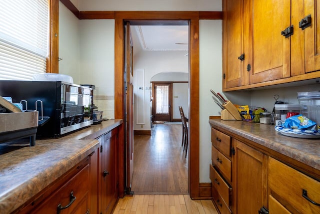 kitchen with light wood finished floors, arched walkways, decorative backsplash, dark countertops, and brown cabinets