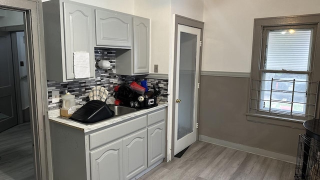 kitchen with light wood-type flooring, tasteful backsplash, white cabinetry, light countertops, and baseboards