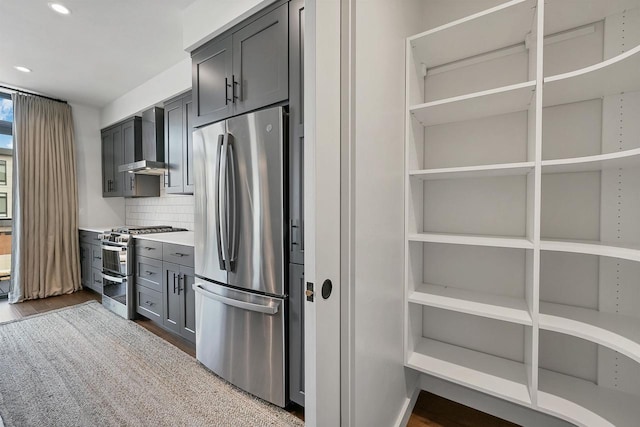 kitchen with dark wood finished floors, stainless steel appliances, light countertops, wall chimney exhaust hood, and tasteful backsplash