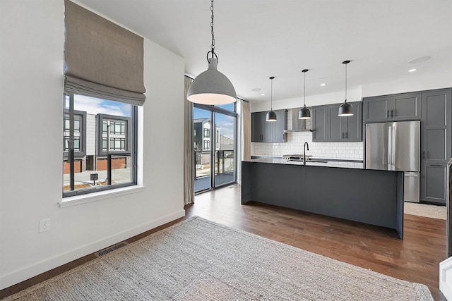 kitchen with tasteful backsplash, visible vents, wall chimney range hood, stainless steel refrigerator, and a sink