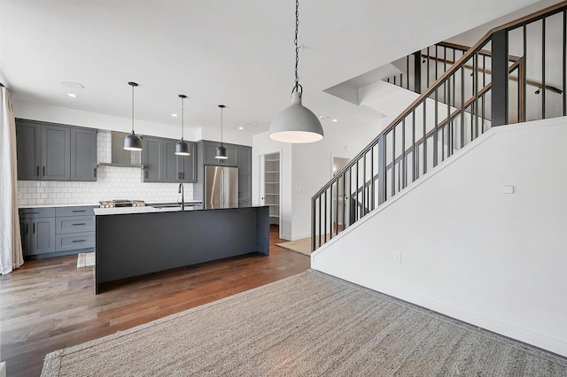 kitchen featuring gray cabinetry, decorative light fixtures, decorative backsplash, wood finished floors, and stainless steel refrigerator