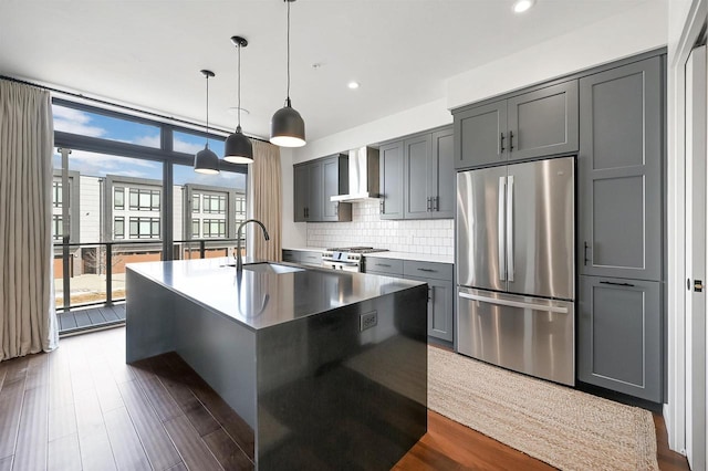 kitchen featuring dark wood-style flooring, gray cabinets, decorative backsplash, appliances with stainless steel finishes, and wall chimney exhaust hood