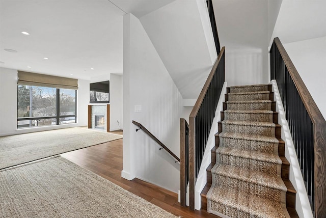 stairway with recessed lighting, a glass covered fireplace, and wood finished floors