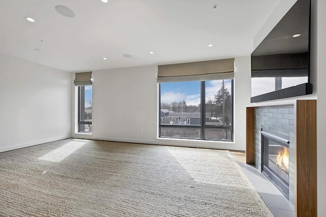 unfurnished living room featuring recessed lighting, baseboards, a fireplace with flush hearth, and a healthy amount of sunlight