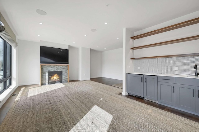 unfurnished living room with wood finished floors, visible vents, recessed lighting, a sink, and a tile fireplace