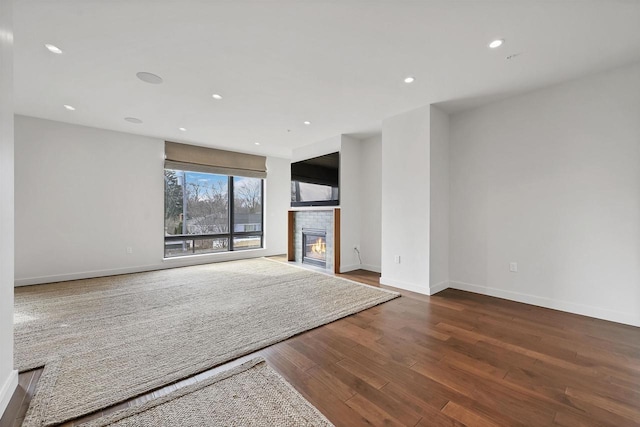 unfurnished living room featuring recessed lighting, a fireplace, baseboards, and wood finished floors