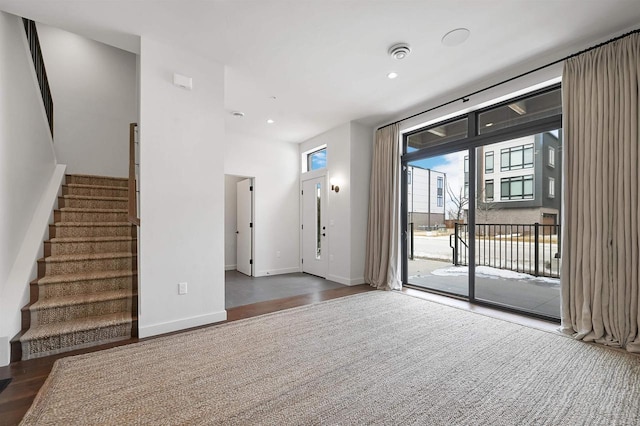 unfurnished living room with wood finished floors, stairway, recessed lighting, and baseboards