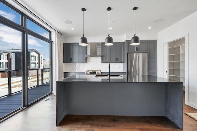 kitchen with stainless steel refrigerator, a sink, dark countertops, dark wood finished floors, and wall chimney range hood