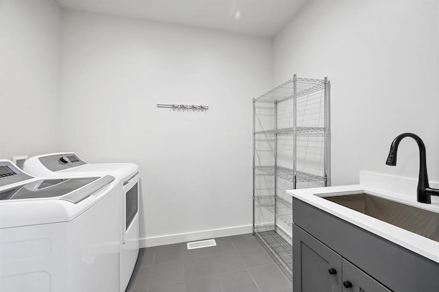 washroom featuring a sink, baseboards, washing machine and dryer, cabinet space, and dark tile patterned flooring