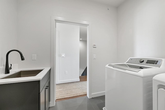 laundry area featuring baseboards, cabinet space, a sink, dark tile patterned floors, and washer and clothes dryer