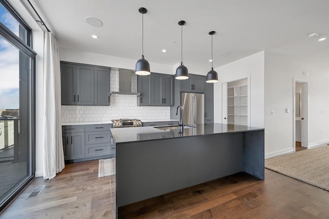 kitchen with wall chimney exhaust hood, a healthy amount of sunlight, freestanding refrigerator, and a sink