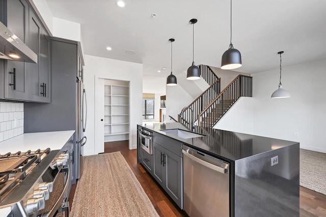 kitchen featuring dark wood finished floors, gray cabinetry, a sink, appliances with stainless steel finishes, and wall chimney range hood