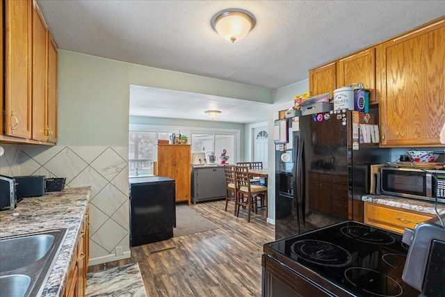 kitchen featuring wood finished floors, brown cabinetry, a sink, black appliances, and light countertops