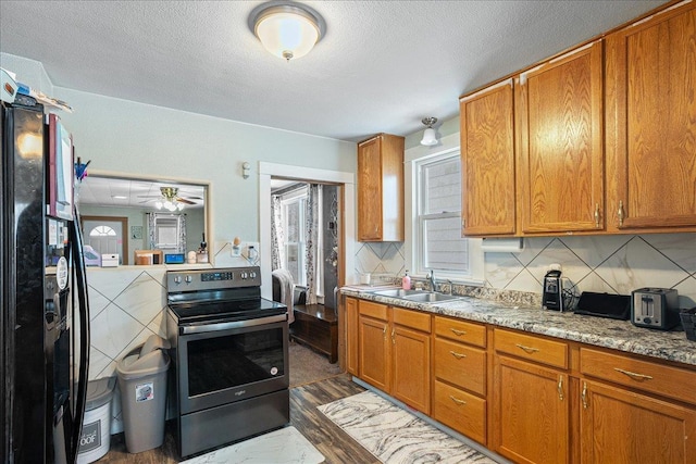 kitchen featuring decorative backsplash, a sink, brown cabinetry, stainless steel electric range oven, and black refrigerator with ice dispenser