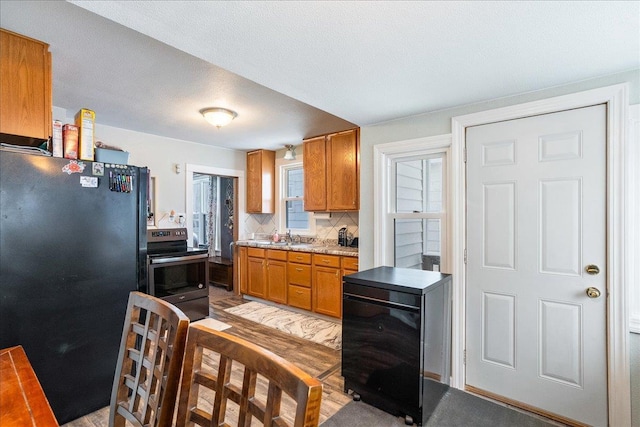 kitchen featuring light countertops, decorative backsplash, freestanding refrigerator, brown cabinetry, and electric range