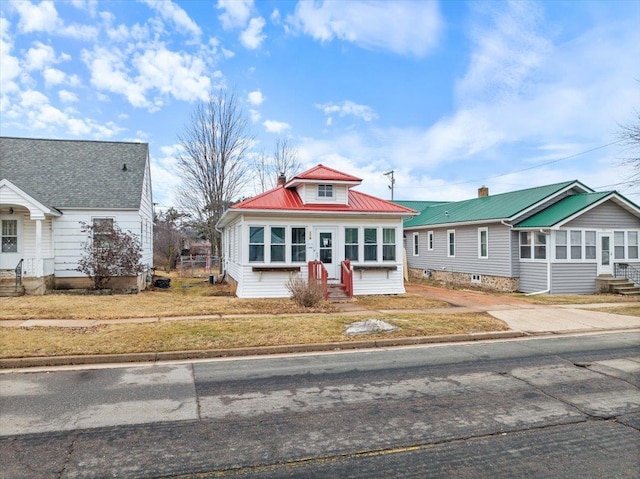 bungalow-style home with entry steps, metal roof, driveway, and a front yard