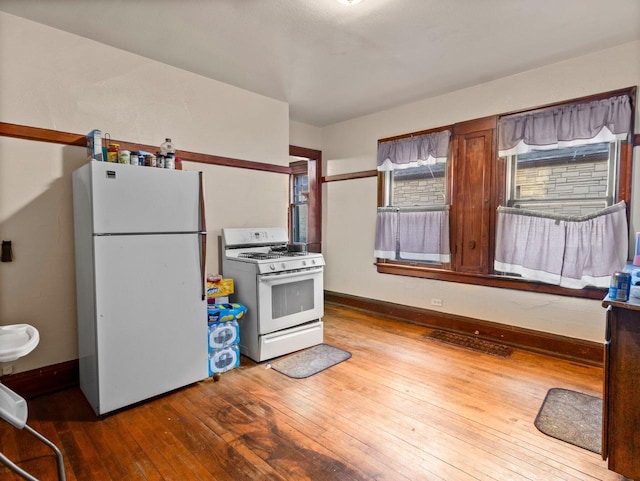 kitchen with hardwood / wood-style floors, white appliances, visible vents, and baseboards