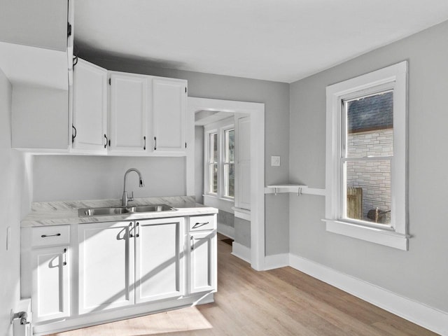 kitchen featuring baseboards, light wood finished floors, a sink, light countertops, and white cabinetry