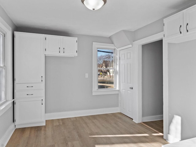 interior space featuring light wood finished floors, white cabinetry, and baseboards