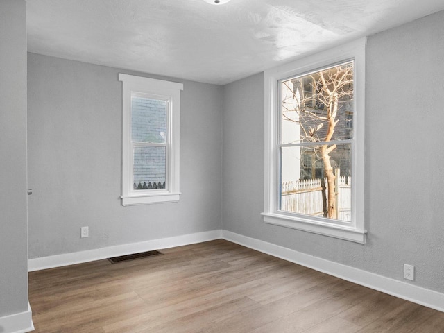 spare room featuring wood finished floors, visible vents, a wealth of natural light, and baseboards