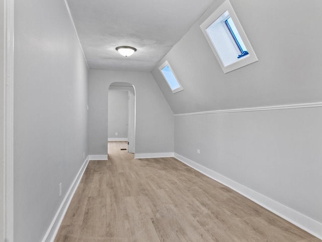 additional living space featuring arched walkways, vaulted ceiling with skylight, light wood finished floors, and baseboards