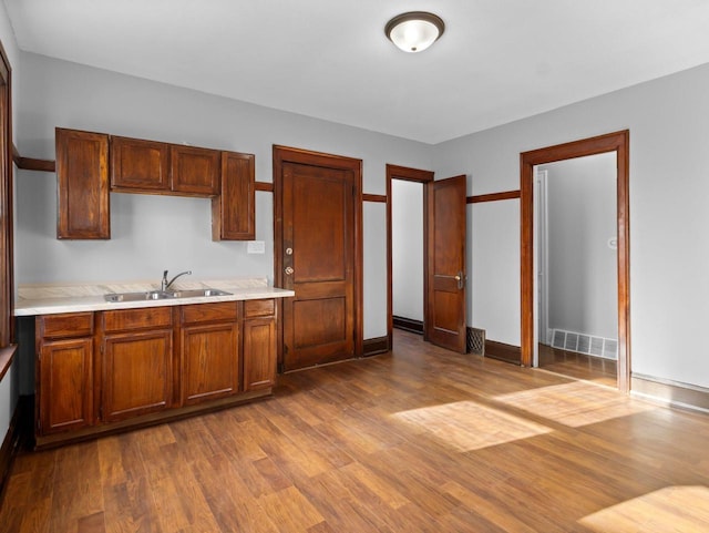 kitchen with baseboards, visible vents, dark wood-style flooring, a sink, and light countertops