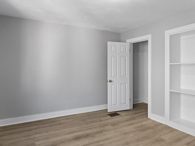 unfurnished bedroom with visible vents, baseboards, a closet, and wood finished floors