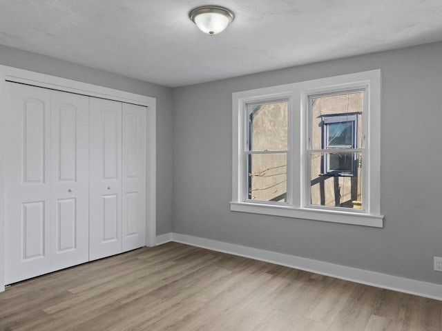 unfurnished bedroom with light wood-type flooring, a closet, and baseboards