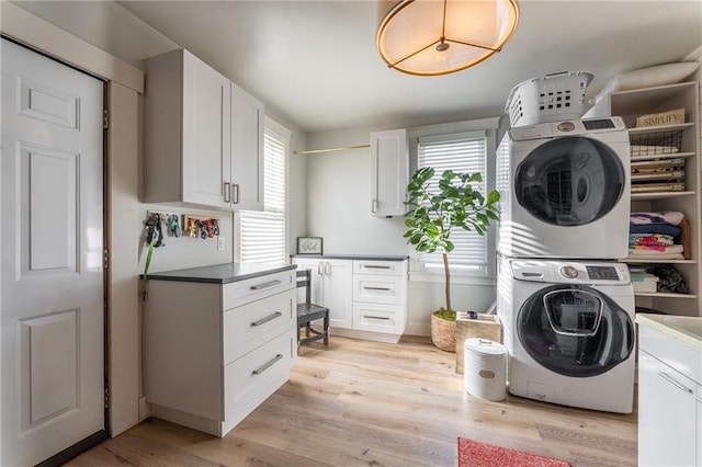 clothes washing area featuring stacked washer and dryer, cabinet space, and light wood-style floors